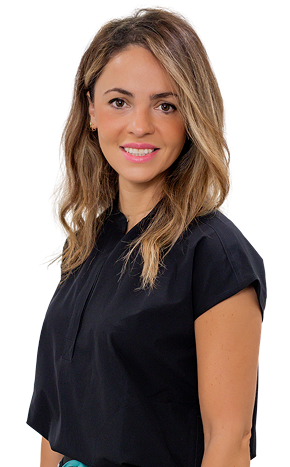 Woman with wavy light brown hair wearing a short-sleeved black blouse, standing and smiling at the camera against a plain white background, embodying confidence in her oral health.