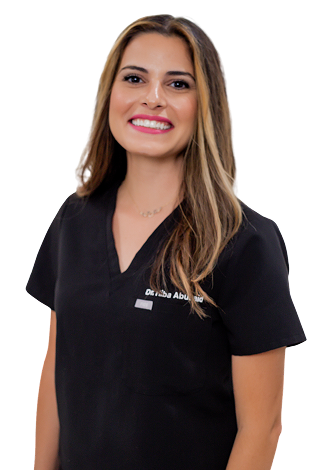 Smiling woman with long hair, wearing black medical scrubs, stands against a plain white background—perfectly capturing the warmth and professionalism of family dentistry.